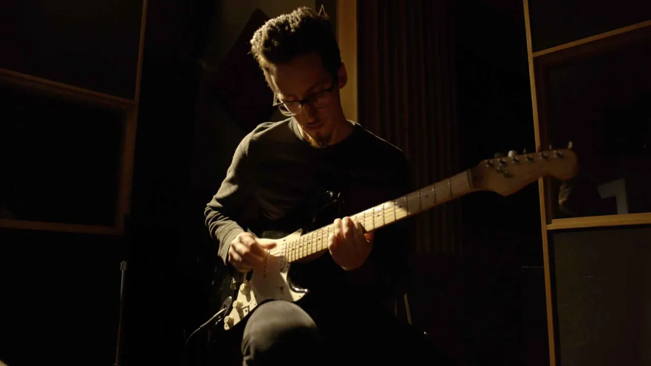 Nate Lanzino playing a black electric guitar in a dimly lit room
